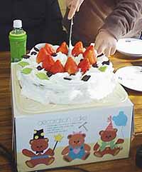 直径30センチはある大きなケーキに入刀している写真。ケーキの上には真っ赤な大粒のイチゴが10個並んでいます。